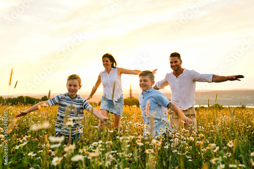 Happy family on daisy field at the sunset having great time together running and fly photo