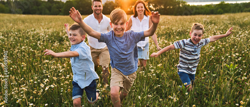Happy family on daisy field at the sunset having great time together running together