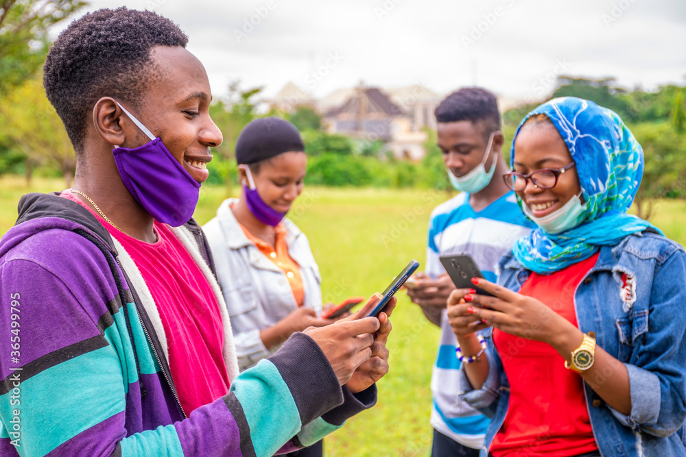a group of young black people using their mobile phones simultaneously, smiling, wearing face masks, with physical distancing a group of young black people using their mobile phones simultaneously, smiling, wearing face masks, with physical distancing