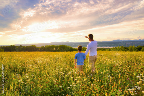 happy family of father and child on field at the sunset having fun pointing something