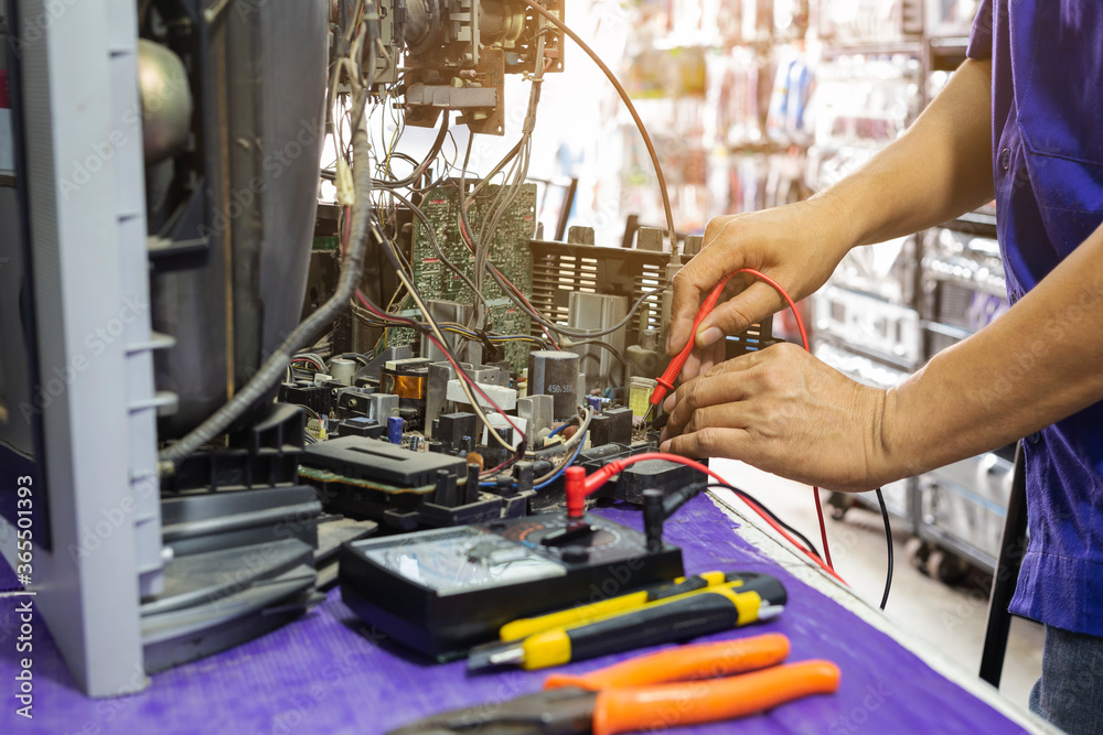 Naklejka premium Close-up of hand's man technician repairing a television. Repairman are checking television circuit board with multimeter. TV repair service center
