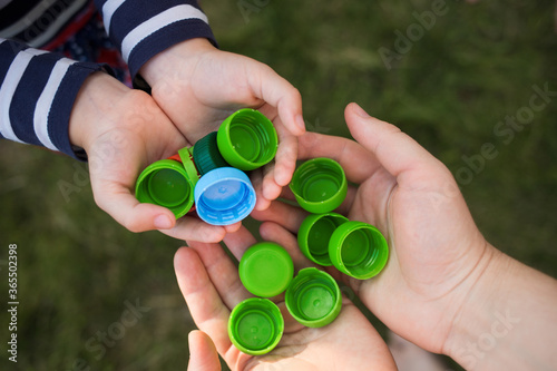 baby puts plastic lids in mother's hands. parent and his child collect cover. recyclable. collecting bottle caps photo