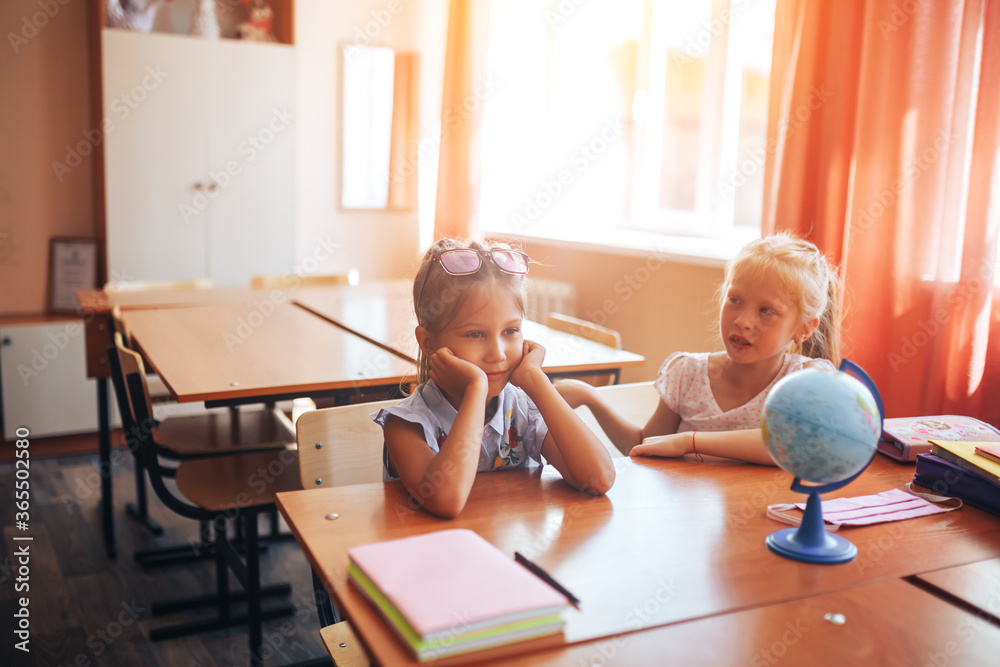 Two schoolgirls are sitting at a school desk, back to school, teaching children