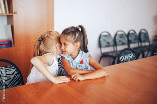 Two schoolgirls sit at a school desk and discuss the purpose of the lesson