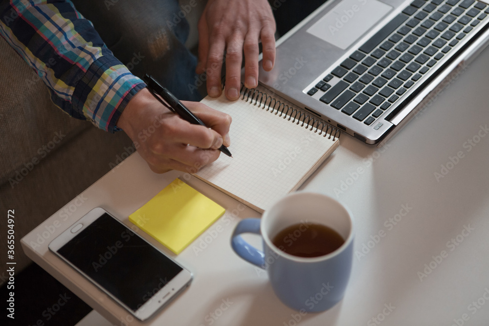 Young man making notices in notebook. Creative freelancer sitting at his working place at home. Close up shot. Top view. Young man making notices in notebook. Creative freelancer sitting at his working place at home. Close up shot. Top view.