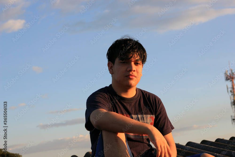 20 year old male model sitting on relaxed rooftop with blue sky in the background