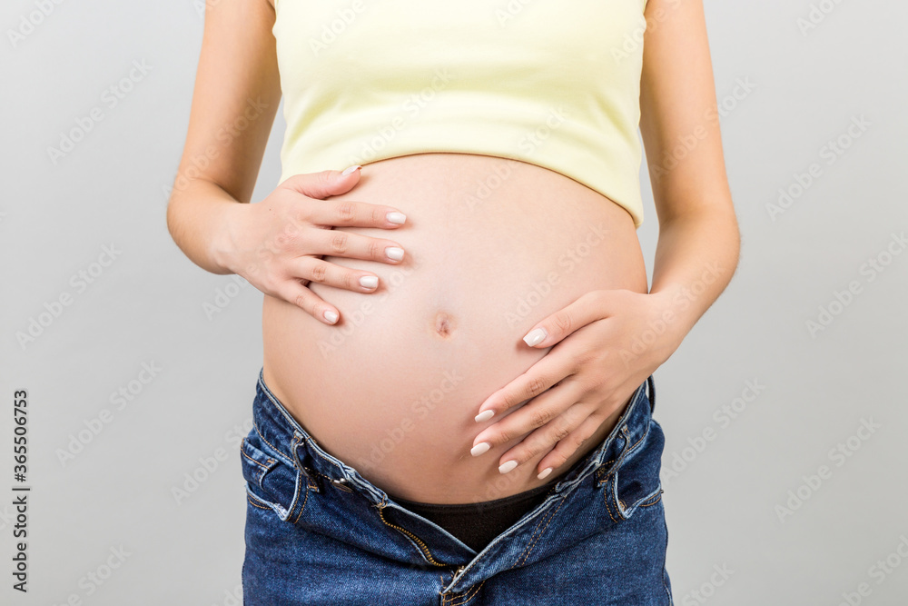 Close up of pregnant belly at colorful background with copy space. Future mother in opened jeans is embracing her naked baby bump. Motherhood concept Close up of pregnant belly at colorful background with copy space. Future mother in opened jeans is embracing her naked baby bump. Motherhood concept