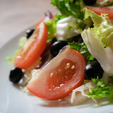 Vegetarian food concept. Healthy fresh vegetable appetizer. Red tomatoes and black olives salad on white plate. Delicious spring meal or refreshment. Close up shot.