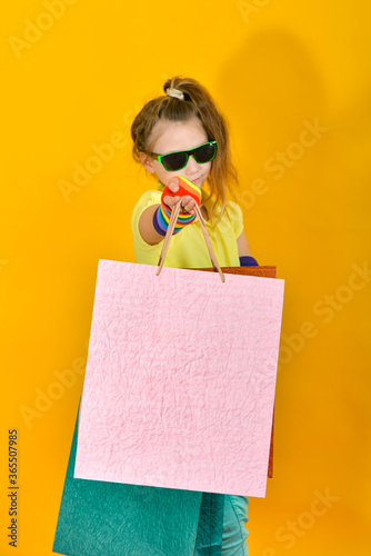 A girl with glasses stands with packages and poses on an orange background.