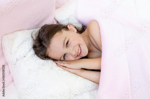 a little girl of 5-6 years old smiles in her sleep, the child lies in bed with her hands folded under her head