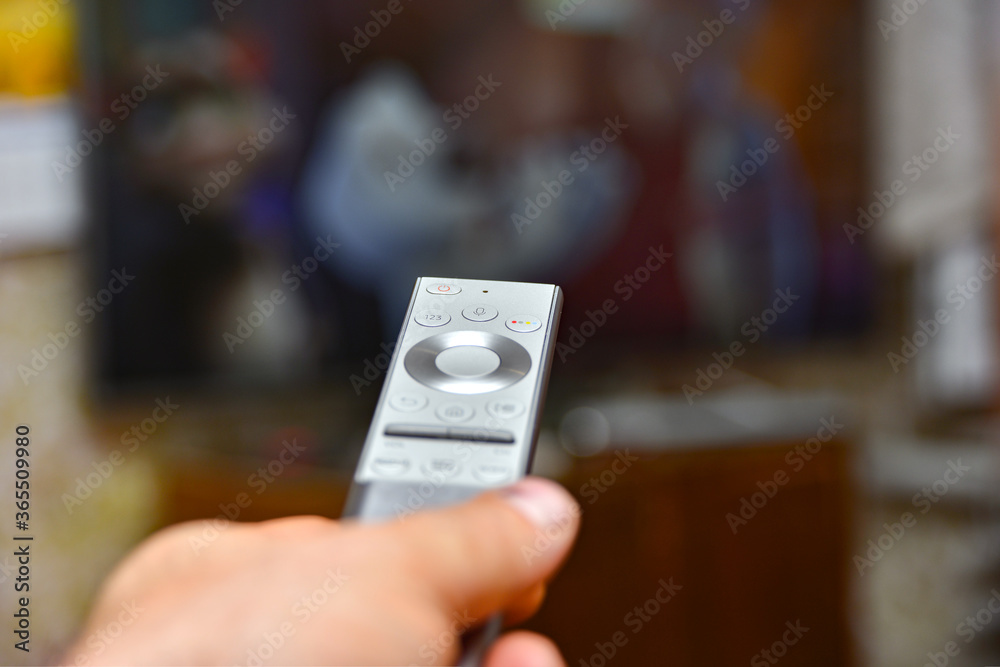 A man holds a remote control in his hand and switches channels to watch TV. Remote control of household appliances. A man holds a remote control in his hand and switches channels to watch TV. Remote control of household appliances.