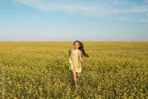 portrait of a teenage girl in a yellow dress running across the field in summer © Alexandr