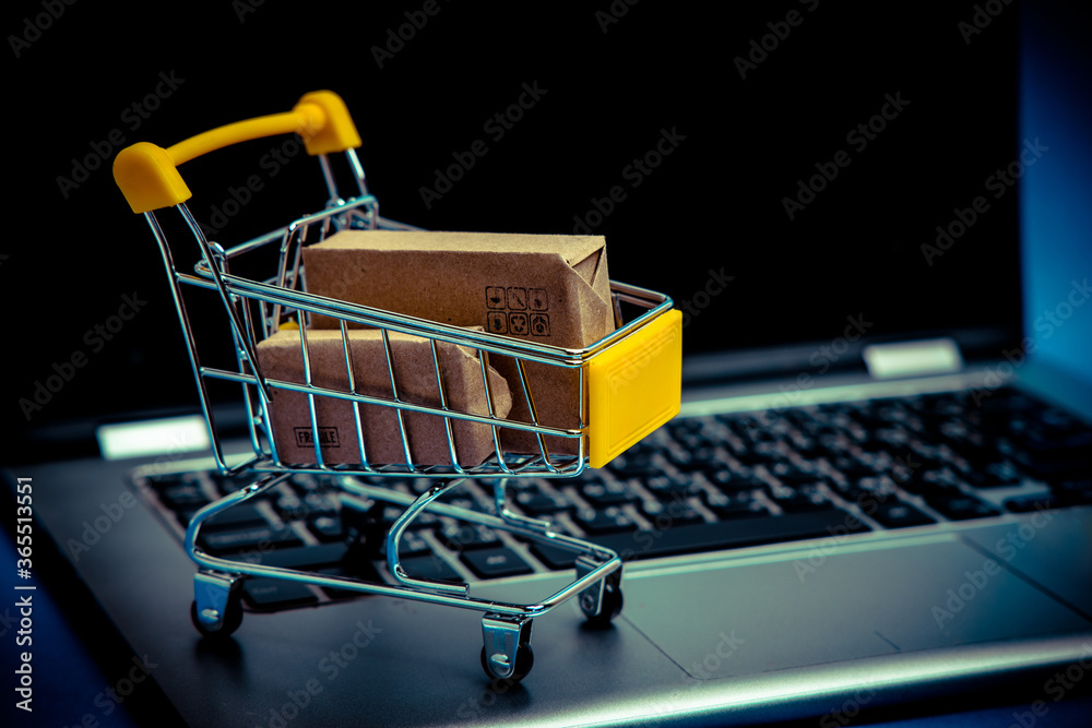 Paper boxes in shopping cart on notebook keyboard. Shopping Online / e-commerce or electronic commerce is a transaction of buying or selling goods or services online over the internet.