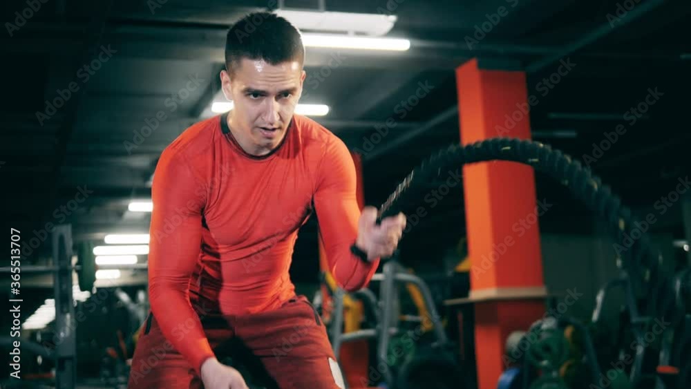 Man workouts with battle ropes in gym.