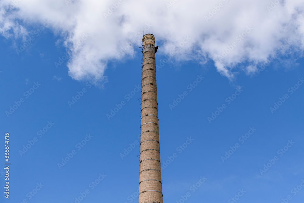 Old brick chimney. Metal clamps reinforcing walls. Background - blue sky with clouds. Concept of industrial technologies of the 19th and 20th centuries.