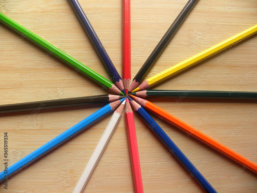 Many color pencils arranged in circle kept on wooden table