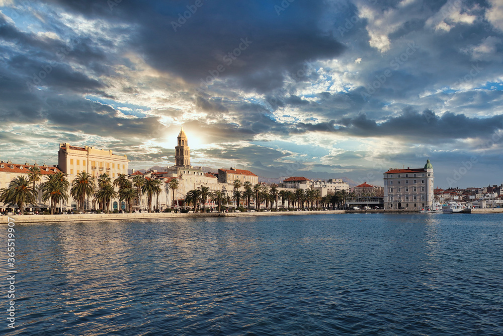 Seaside view of the town of Split, Croatia. Riviera with trees and the old town with the saint dominus cathedral belltower peeking above the buildings. Beautiful dramatic sunset lined up with tower