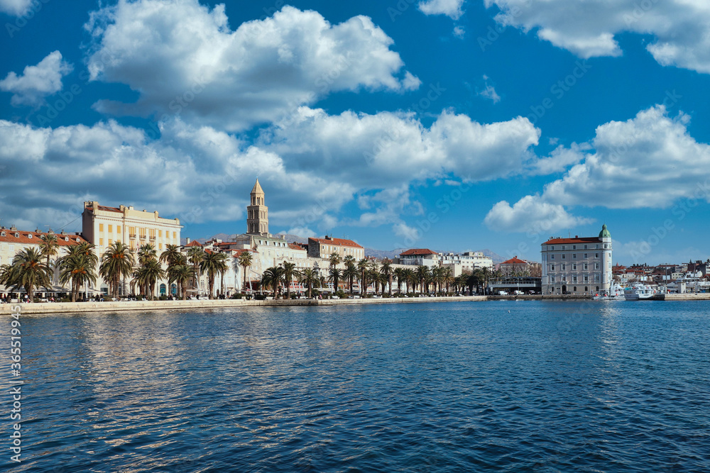 Seaside view of the town of Split, Croatia. Riviera with trees and the old town with the saint dominus cathedral belltower peeking above the buildings. Beautiful blue mid day sky