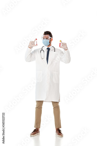 Doctor in safety goggles and mask holding test tubes with blood samples on white background