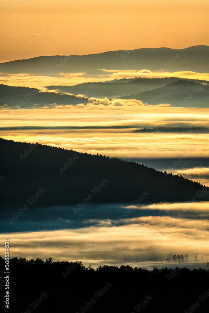 Obraz premium A hazy sunrise in the mountains. Mountains silhouettes and fog in the valleys. Photo from Polonina Wetlinska. Bieszczady National Park. Carpathians. Poland.