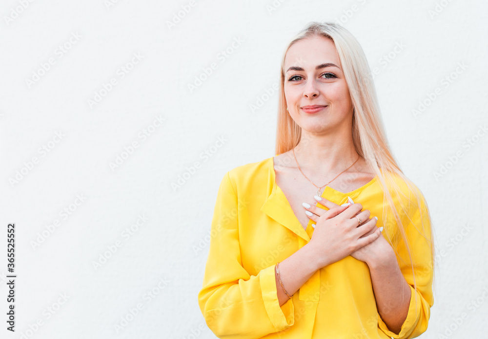 Beautiful positive friendly-looking young woman with lovely sincere smile feeling thankful and grateful, showing her heart filled with love and gratitude holding hands on her breast Beautiful positive friendly-looking young woman with lovely sincere smile feeling thankful and grateful, showing her heart filled with love and gratitude holding hands on her breast