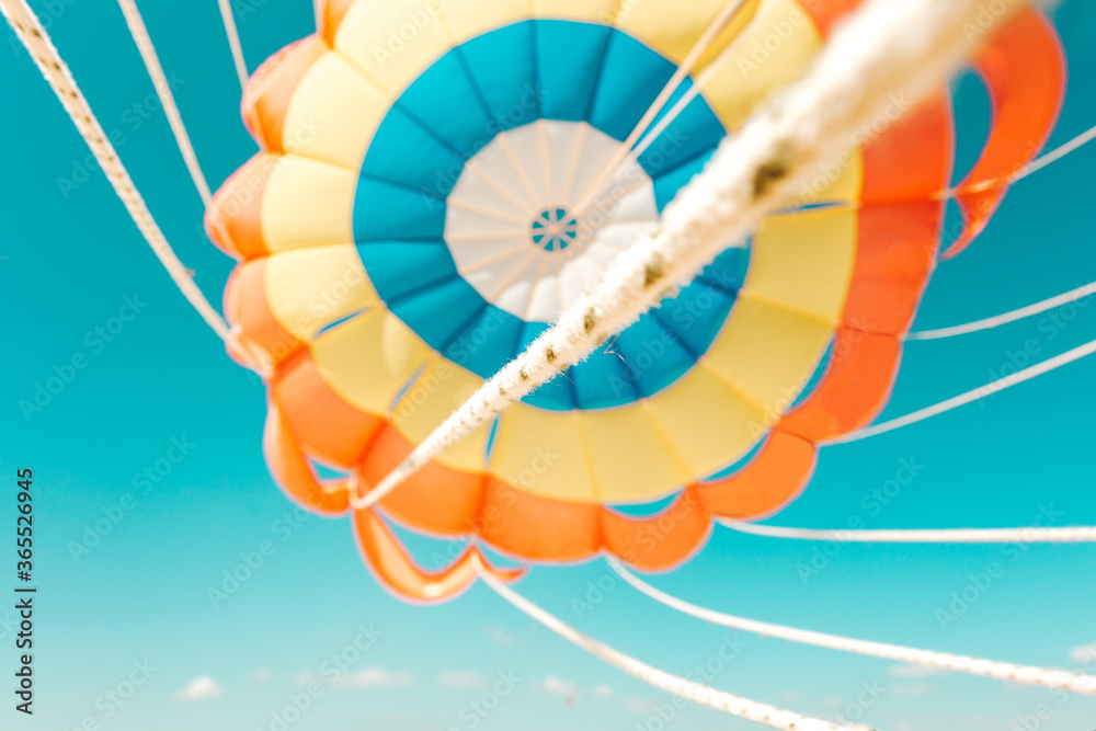 Fototapeta premium Parachute parasailing of tourists on a sandy beach Sunny weather against the background of clear sea and ocean.The wind blows up the canopy of the parachute against a clear blue sky with clouds