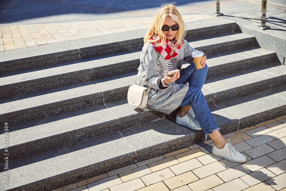 Smiling woman wearing blue jeans and grey coat spending time outdoors