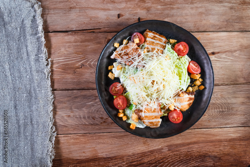 Appetizing Caesar salad with chicken in a black plate on a wooden table. The concept of healthy food and serving