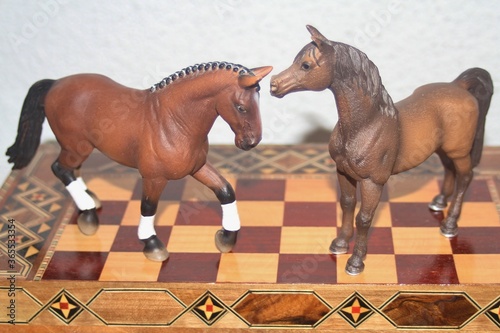 Dos caballos castaños de juguete sobre tablero de ajedrez artesanal sirio photo