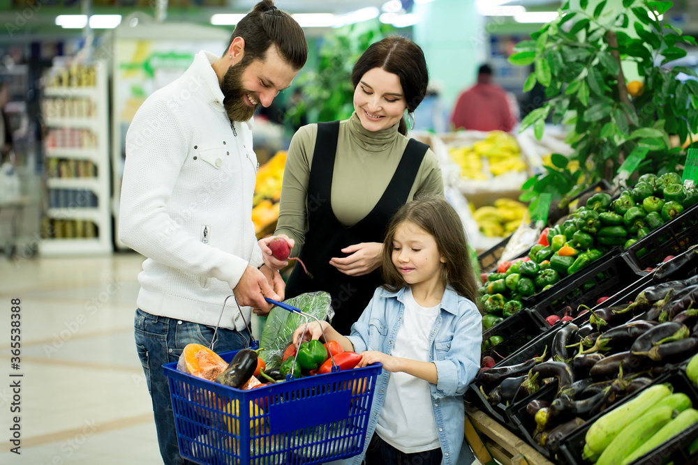 a woman with a man and a child, choosing vegetables while shopping in a vegetable supermarket
