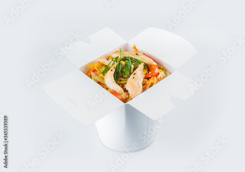 Isolated Asian Ramen Noodles with chicken fillet, vegetables, soy sauce and spring onion scallions in white carton takeaway delivery box. Food delivery package with ready to eat dish inside
