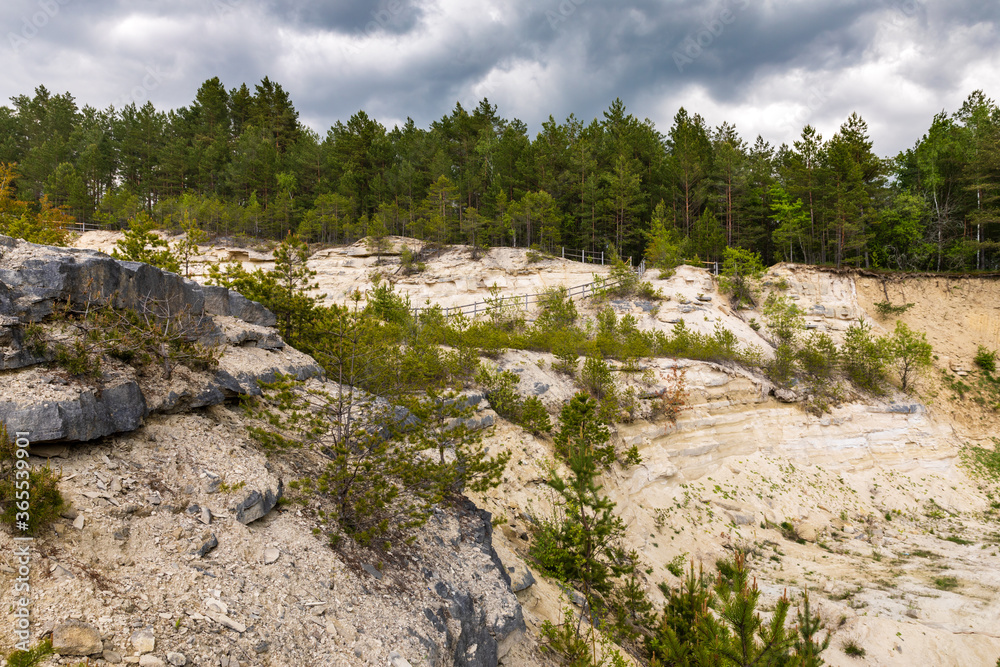 Limestone wall with forest on top and dark cloudy, stormy sky above. Landscape of former rock quarry in Nowiny, Susiec, Poland, Europe. Limestone wall with forest on top and dark cloudy, stormy sky above. Landscape of former rock quarry in Nowiny, Susiec, Poland, Europe.