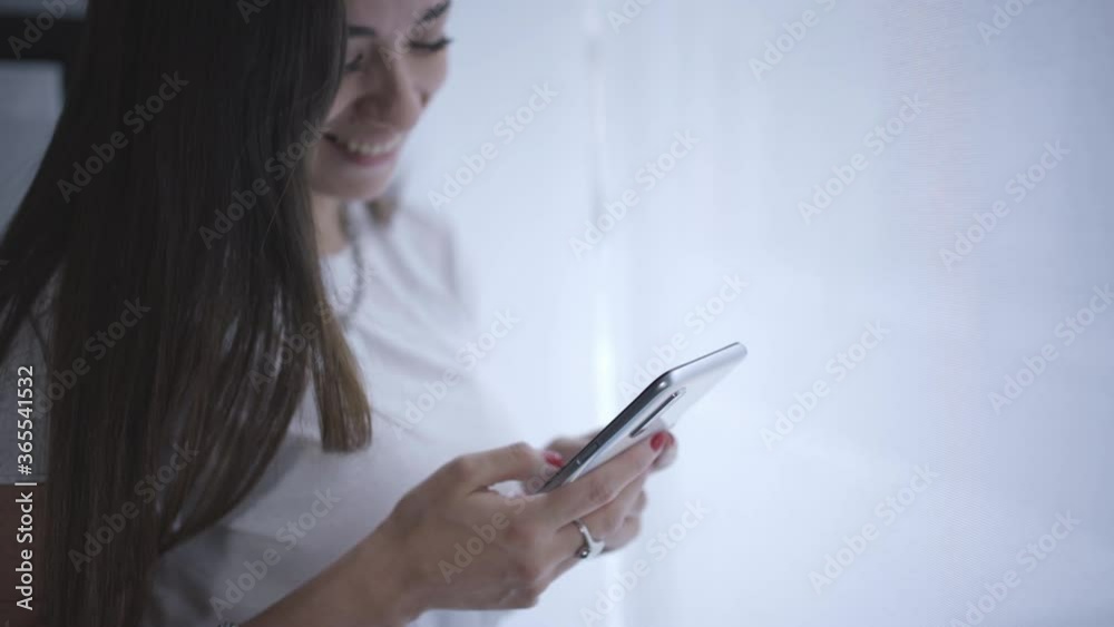 Beautiful young woman sitting by window using a smartphone. Texting, scrolling, tapping, sharing messages on social media, enjoying mobile technology making use of apps Beautiful young woman sitting by window using a smartphone. Texting, scrolling, tapping, sharing messages on social media, enjoying mobile technology making use of apps