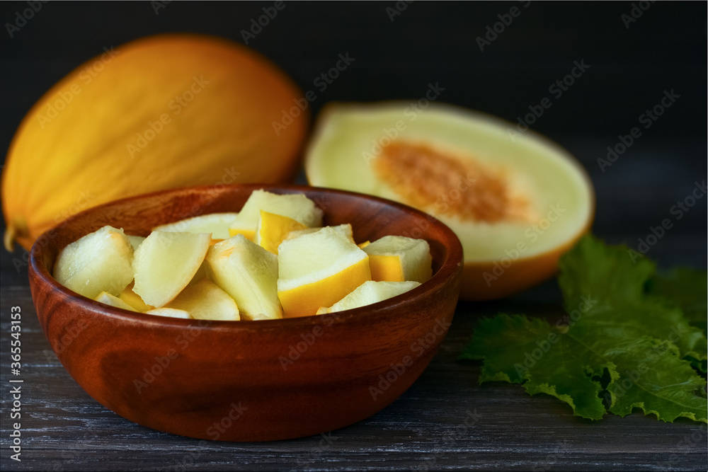 slices of cut melon in a wooden bowl close-up. background with melon slices in a bowl and a whole melon on the table. slices of cut melon in a wooden bowl close-up. background with melon slices in a bowl and a whole melon on the table.