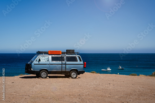 Camper van parked on the beach in front of the blue sea during holidays