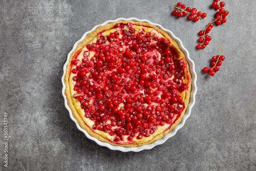 Redcurrant cheesecake, tart with fresh berries in a white baking dish. Dark gray background. Top view.
