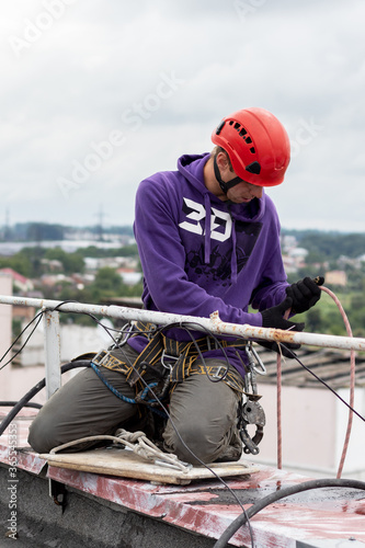 Worker fixes a climbing equipment before descending from roof. Industrial alpinism.