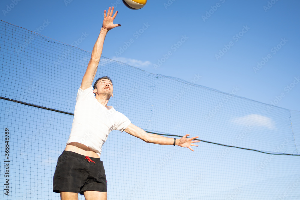 The guy hits the volleyball in the air against the background of the sky and the net. Outdoor volleyball game