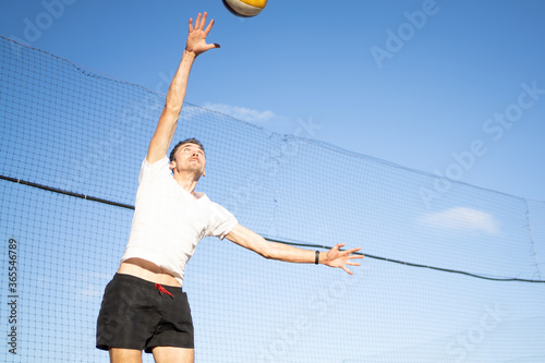 The guy hits the volleyball in the air against the background of the sky and the net. Outdoor volleyball game © Alex