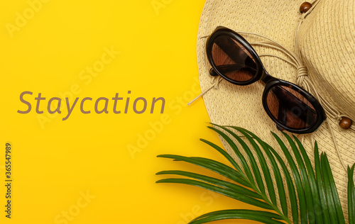 Creative composition on the theme of summer holidays. Hat, glasses and palm branch on a yellow background. Text a STAYCATION. The concept of holiday, vacation, travel photo