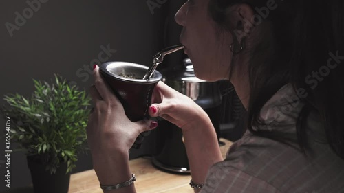 Beautiful young woman drinking Argentinean Mate (Mate Argentino). Traditional infusion beverage common in Argentina, Uruguay, Paraguay  and Brazil. Girl from Argentina holds ad drinks Mate with straw
