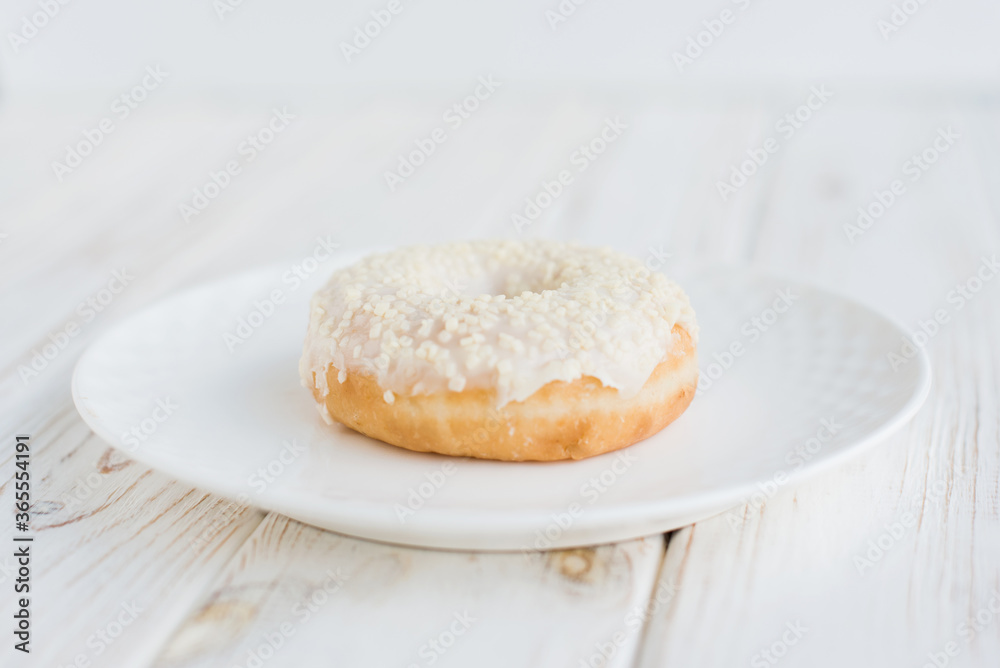 Close-up view of donut on a small white plate with white background. Fresh sweet colorful homemade vanilla donuts on vintage background for birthday or party, with free space for text
