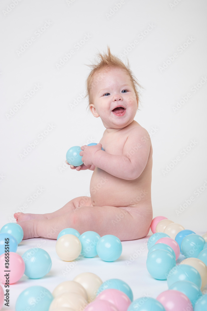 11 month old baby girl on a white background in the studio playing with toy balls