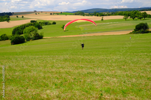 paradigler scatters a beautiful green summer field, green hills, shrubs, trees, concept parawaiting, paragliding, coast, ecology, environmental protection