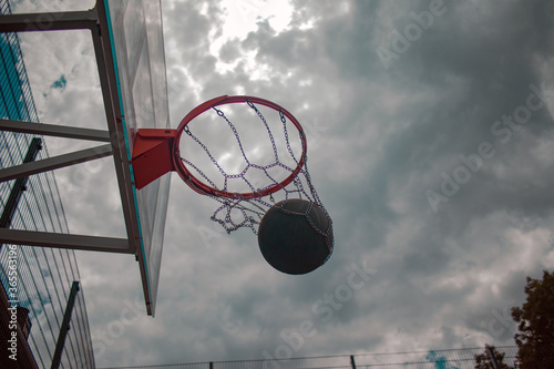 dark basketball ball on sky background near basketball basket bottom view