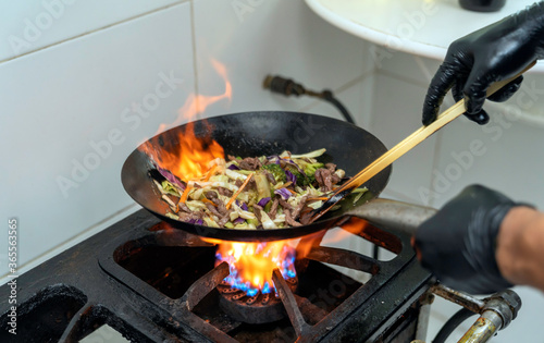Chef making japonese food. Stir-fry soba noodles with beef and vegetables in wok pan on dark background photo