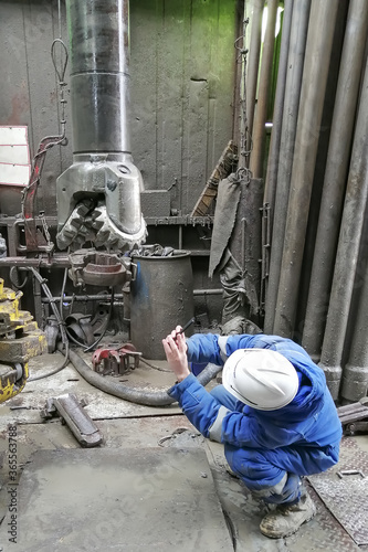 A drill bit specialist examines the condition of a bit pulled out of an oil and gas well. The engineer is wearing a blue overalls and a white hard hat.