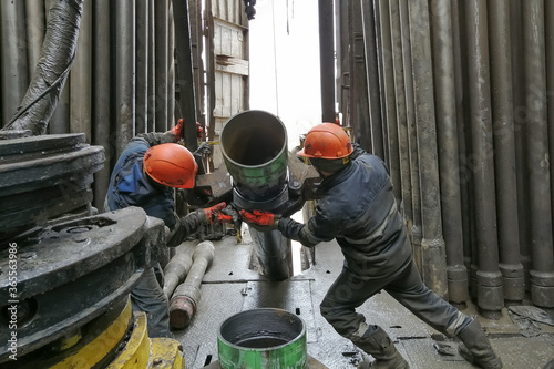 Two drilling crew workers dismantle the bottom of the drill string. Unscrewing the spiral calibrator. Working with a machine key. They are located on the rotary platform of the drilling rig.