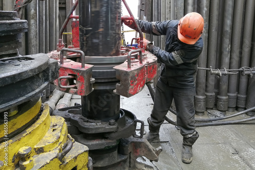 A drilling worker makes up pipes to run the casing into the well with a pneumatic wrench. It is located on the rotary platform of the drilling rig. photo