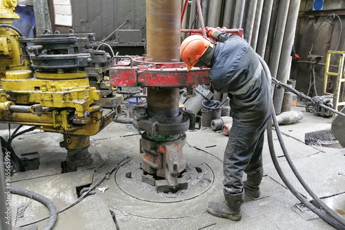 A drilling worker makes up pipes to run the casing into the well with a pneumatic wrench. It is located on the rotary platform of the drilling rig. photo